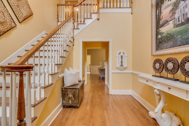 stairway featuring a high ceiling, baseboards, and wood finished floors