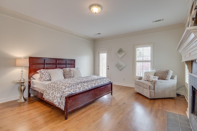 bedroom featuring wood finished floors, baseboards, visible vents, a fireplace with flush hearth, and ornamental molding