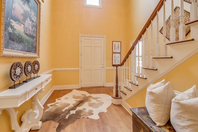 entrance foyer with visible vents, baseboards, stairway, a towering ceiling, and wood finished floors