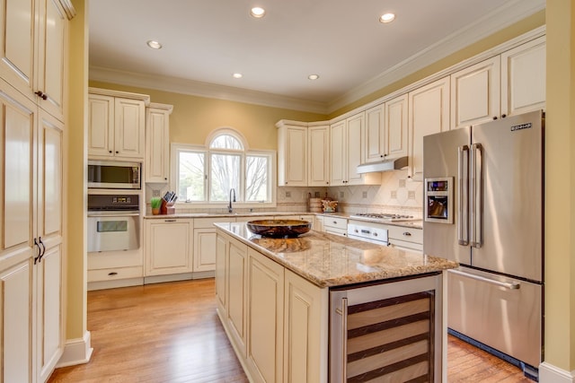 kitchen with beverage cooler, light wood finished floors, ornamental molding, under cabinet range hood, and appliances with stainless steel finishes