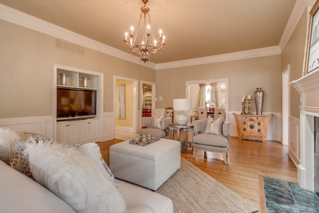 living room featuring light wood-type flooring, visible vents, a wainscoted wall, a premium fireplace, and a chandelier