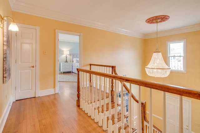 corridor with an upstairs landing, baseboards, light wood-style floors, and ornamental molding