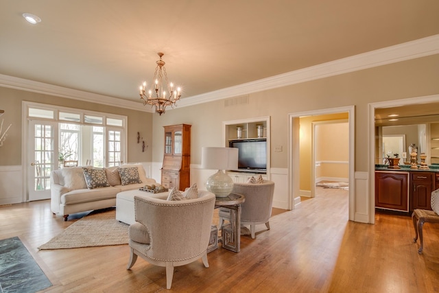 living room with light wood-type flooring, a wainscoted wall, visible vents, ornamental molding, and a chandelier