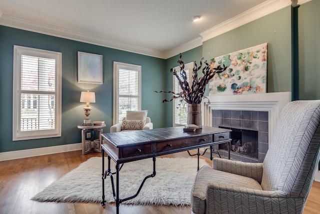 office with baseboards, wood finished floors, a tiled fireplace, and crown molding