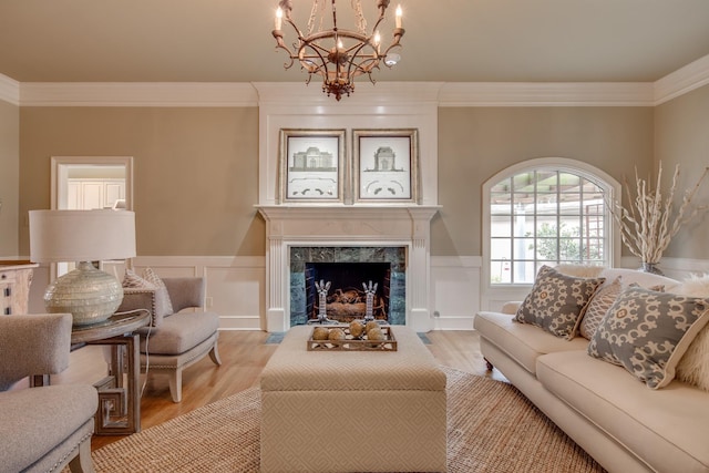 living room featuring crown molding, light wood-style flooring, a wainscoted wall, and a premium fireplace