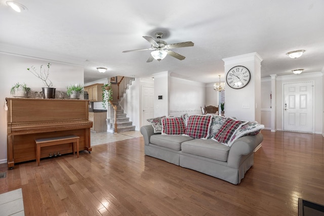 living area featuring stairway, baseboards, light wood-style flooring, ornamental molding, and ceiling fan with notable chandelier