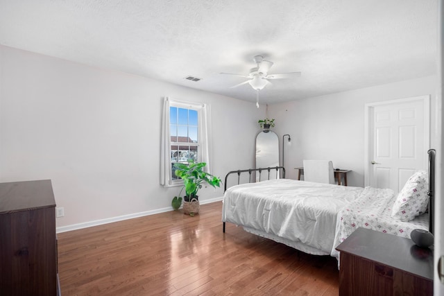 bedroom with visible vents, ceiling fan, baseboards, wood finished floors, and a textured ceiling