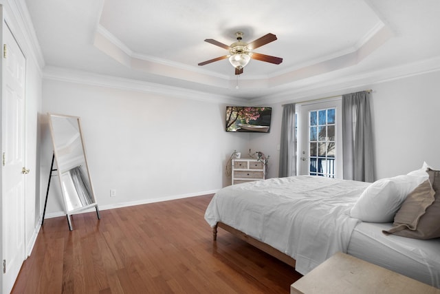 bedroom featuring a tray ceiling, baseboards, wood finished floors, and crown molding