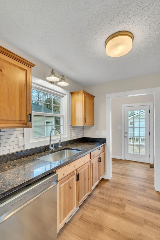 kitchen featuring tasteful backsplash, dishwasher, dark stone counters, light wood-type flooring, and a sink