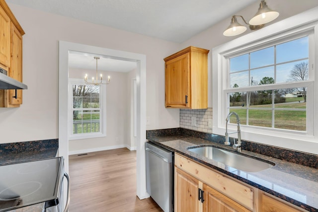 kitchen featuring dark stone counters, a sink, light wood-style floors, dishwasher, and backsplash