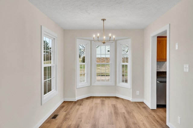 unfurnished dining area with light wood-type flooring, visible vents, a textured ceiling, baseboards, and a chandelier