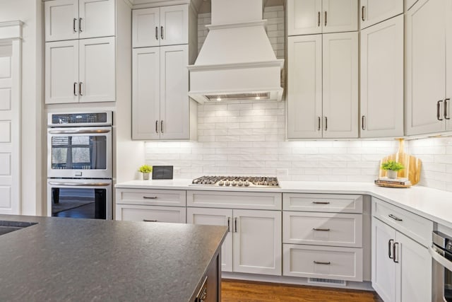 kitchen with visible vents, stainless steel appliances, dark wood-type flooring, custom range hood, and backsplash