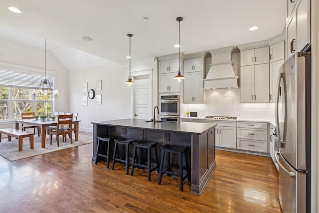 kitchen featuring a breakfast bar area, stainless steel appliances, decorative backsplash, vaulted ceiling, and custom range hood