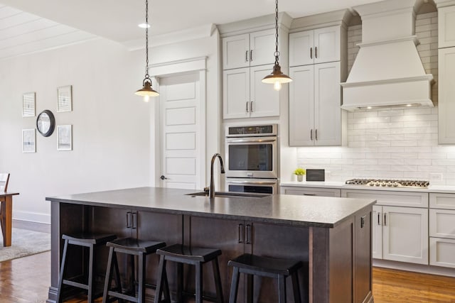 kitchen featuring a breakfast bar, custom exhaust hood, stainless steel appliances, dark wood-type flooring, and tasteful backsplash