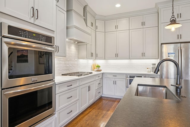 kitchen with custom range hood, a sink, wood finished floors, stainless steel appliances, and hanging light fixtures