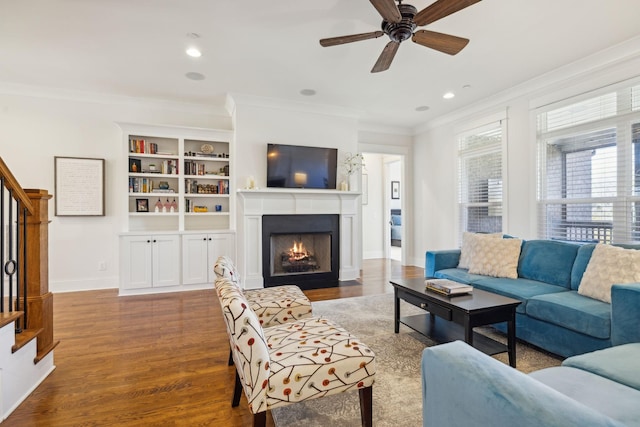 living room featuring crown molding, baseboards, a fireplace with flush hearth, stairs, and wood finished floors