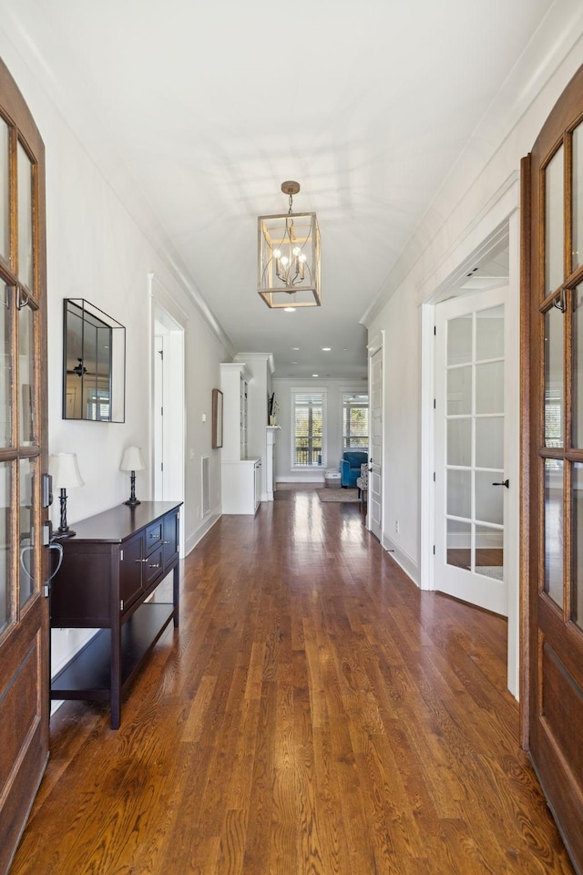 corridor with a chandelier, baseboards, ornamental molding, and dark wood-style flooring