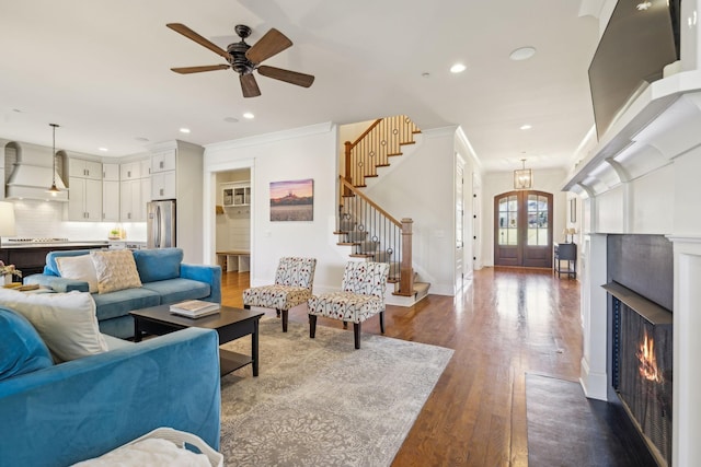 living area featuring stairway, dark wood-style floors, a warm lit fireplace, french doors, and crown molding