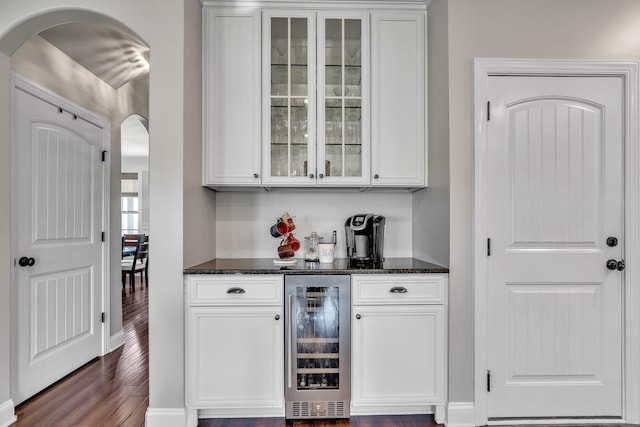 bar featuring arched walkways, dark wood-type flooring, beverage cooler, and a dry bar