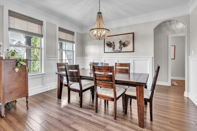 dining area with a decorative wall, ornamental molding, wood finished floors, arched walkways, and a notable chandelier