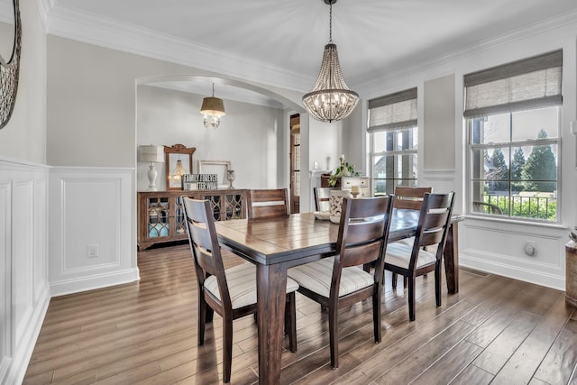 dining room with wood finished floors, arched walkways, a chandelier, and a decorative wall