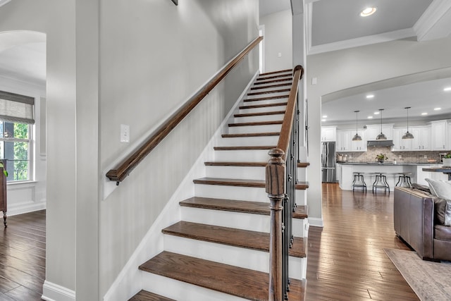 staircase featuring recessed lighting, arched walkways, wood-type flooring, and ornamental molding