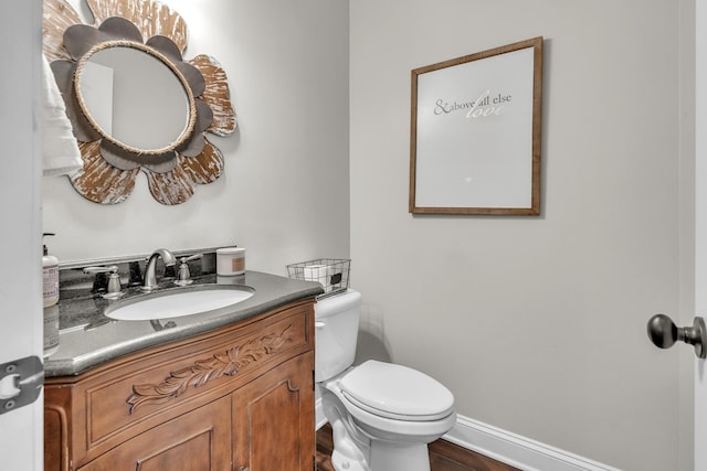 half bathroom featuring toilet, vanity, baseboards, and wood finished floors