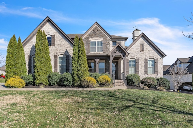 french country home featuring brick siding, a chimney, and a front lawn