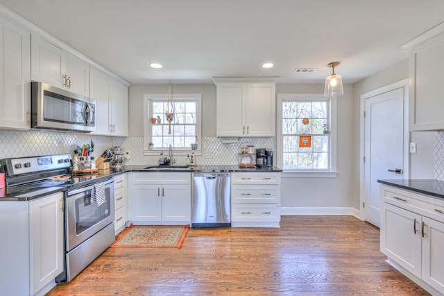 kitchen featuring dark countertops, light wood-style floors, white cabinets, stainless steel appliances, and a sink