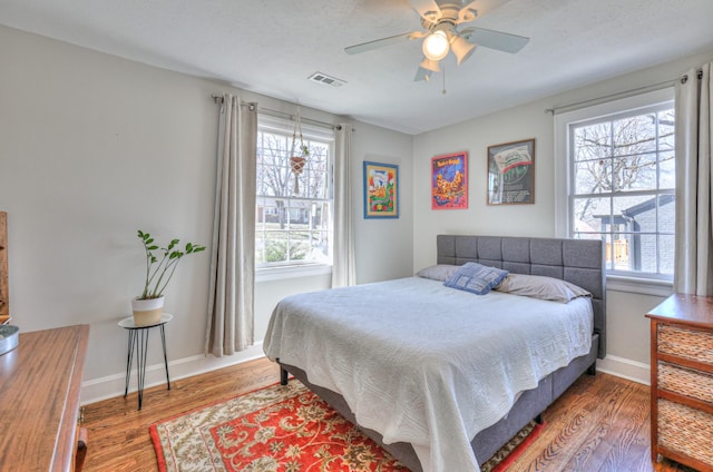 bedroom featuring visible vents, multiple windows, baseboards, and wood finished floors