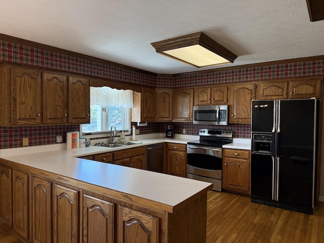 kitchen with hardwood / wood-style flooring, a sink, appliances with stainless steel finishes, a peninsula, and light countertops