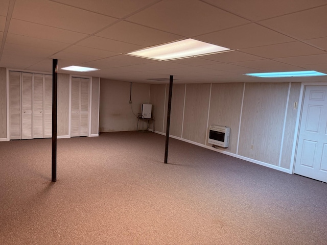 finished basement featuring a paneled ceiling, heating unit, baseboards, and carpet flooring