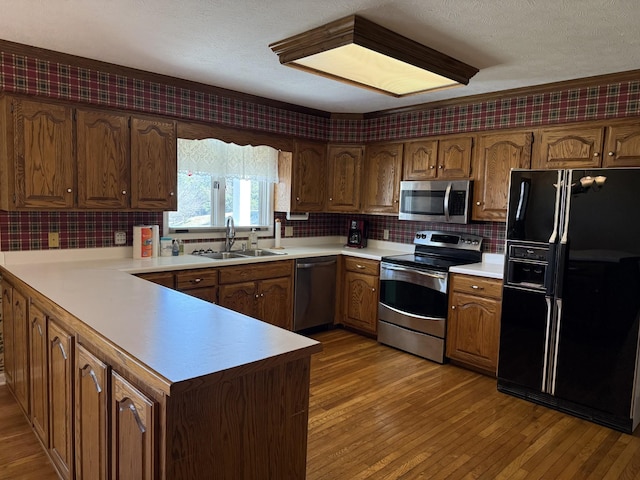 kitchen featuring light wood-type flooring, light countertops, a peninsula, stainless steel appliances, and a sink