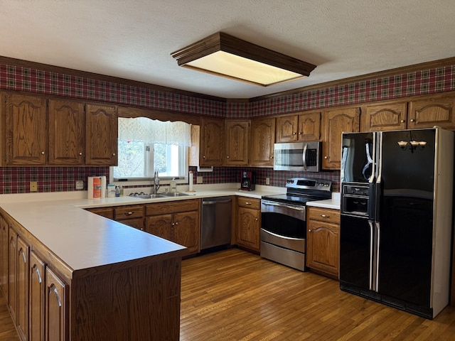 kitchen with light wood-type flooring, a sink, appliances with stainless steel finishes, a peninsula, and wallpapered walls