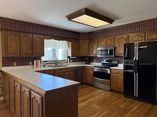 kitchen featuring appliances with stainless steel finishes, wood-type flooring, a peninsula, and a sink