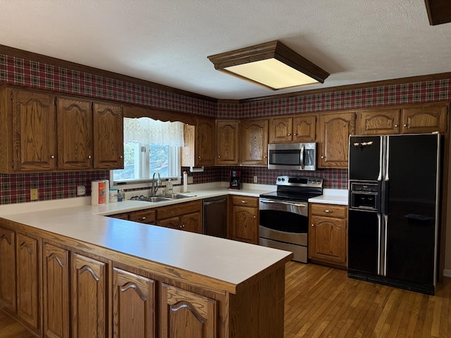 kitchen featuring appliances with stainless steel finishes, light countertops, a peninsula, and a sink