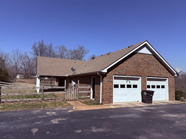 view of front of house featuring fence, brick siding, driveway, and a shingled roof