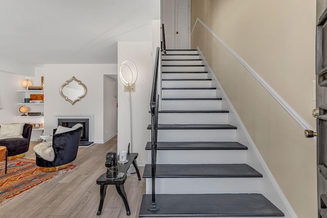 stairway with wood finished floors and a fireplace with raised hearth