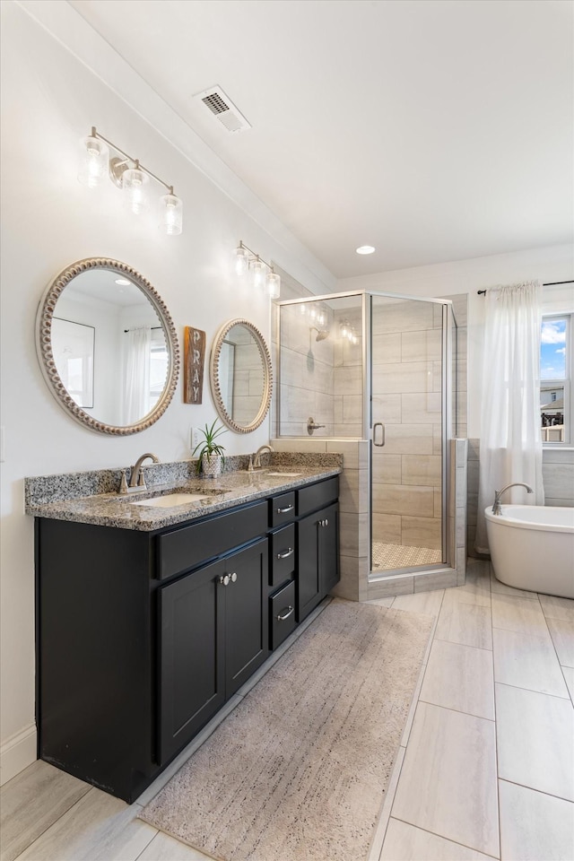 bathroom featuring visible vents, a stall shower, a sink, double vanity, and a soaking tub