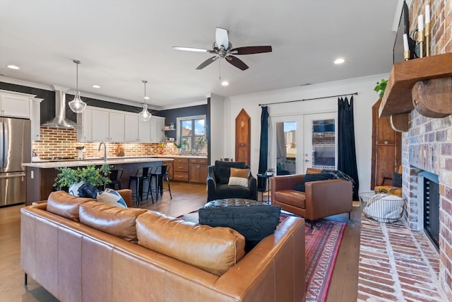 living room featuring light wood-style flooring, recessed lighting, a fireplace, ornamental molding, and french doors