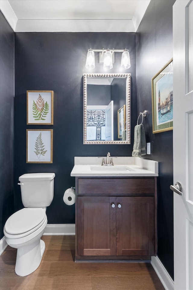 bathroom featuring baseboards, toilet, wood finished floors, and vanity