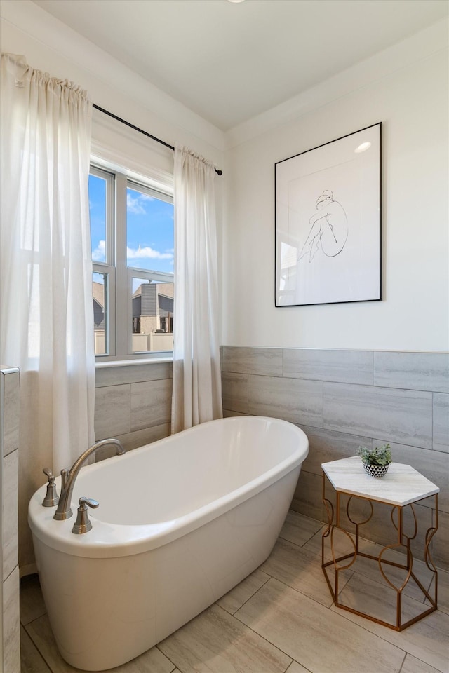 bathroom with wainscoting, a freestanding bath, and tile walls