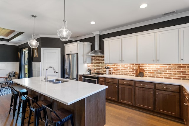 kitchen with ornamental molding, a sink, wall chimney range hood, appliances with stainless steel finishes, and light countertops