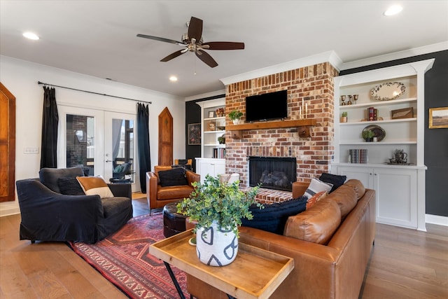 living area with light wood-style flooring, french doors, ornamental molding, and a brick fireplace