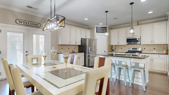 kitchen with dark countertops, appliances with stainless steel finishes, a kitchen island with sink, and crown molding