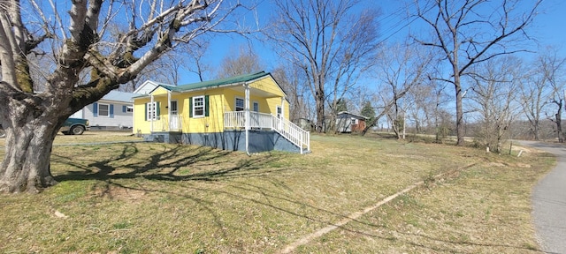 view of side of home featuring covered porch, a lawn, and stairs