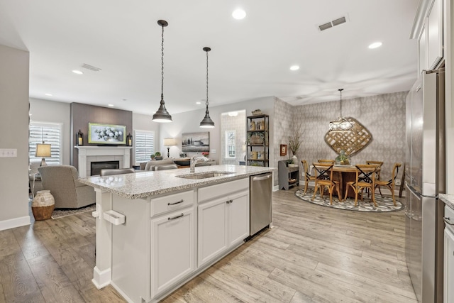 kitchen featuring wallpapered walls, light wood-type flooring, a fireplace, stainless steel appliances, and a sink