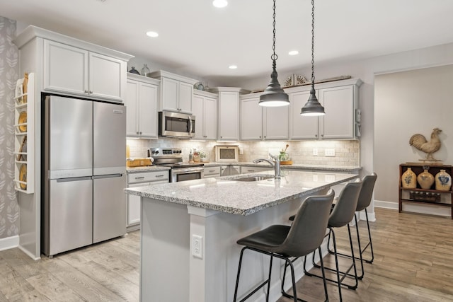 kitchen with a sink, stainless steel appliances, light wood-type flooring, and tasteful backsplash