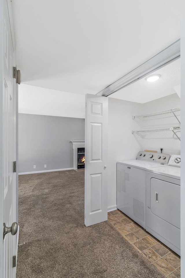 clothes washing area with a warm lit fireplace, washing machine and dryer, carpet floors, baseboards, and laundry area