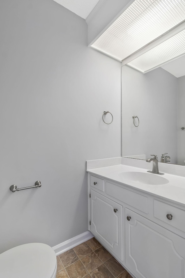 half bathroom with baseboards, toilet, and vanity